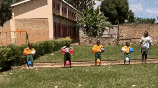 Four nursery school children hopping down the field with balloons under their arms and between their legs.