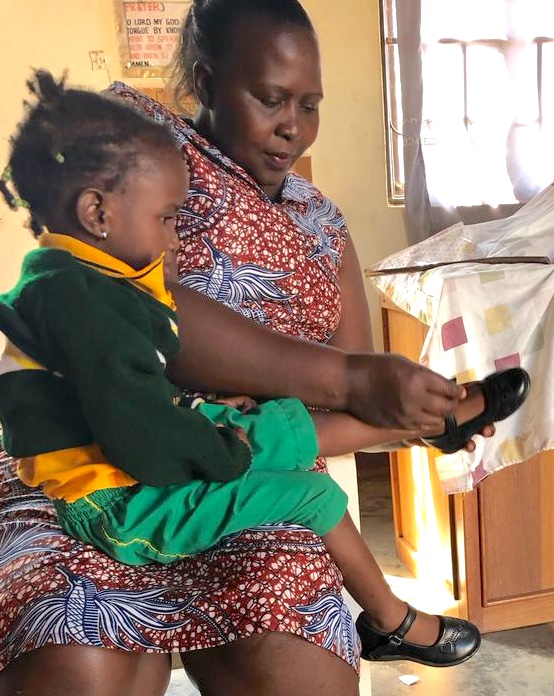 Ugandan woman (nursery school teacher) with a child on her lap, trying on new shoes