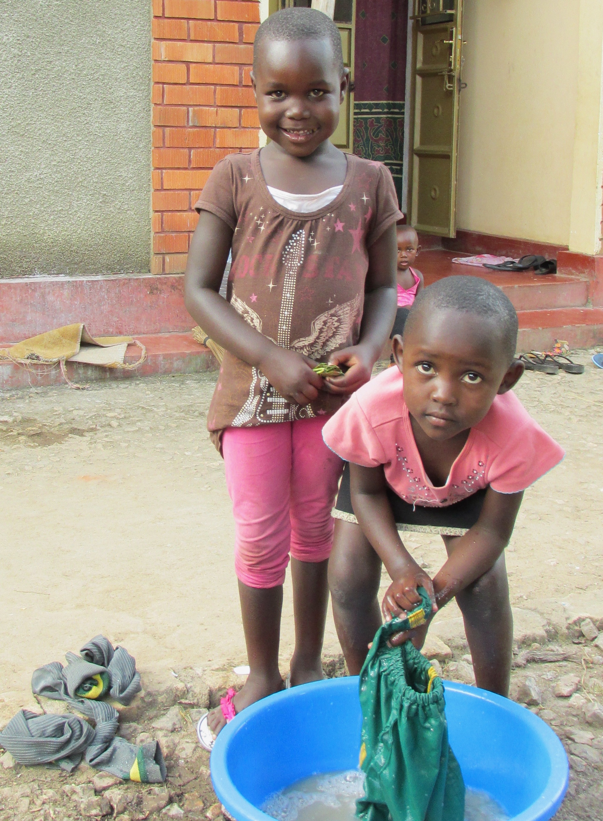 Two young girls by a laundry tub. One is scrubbing her school uniform shorts.