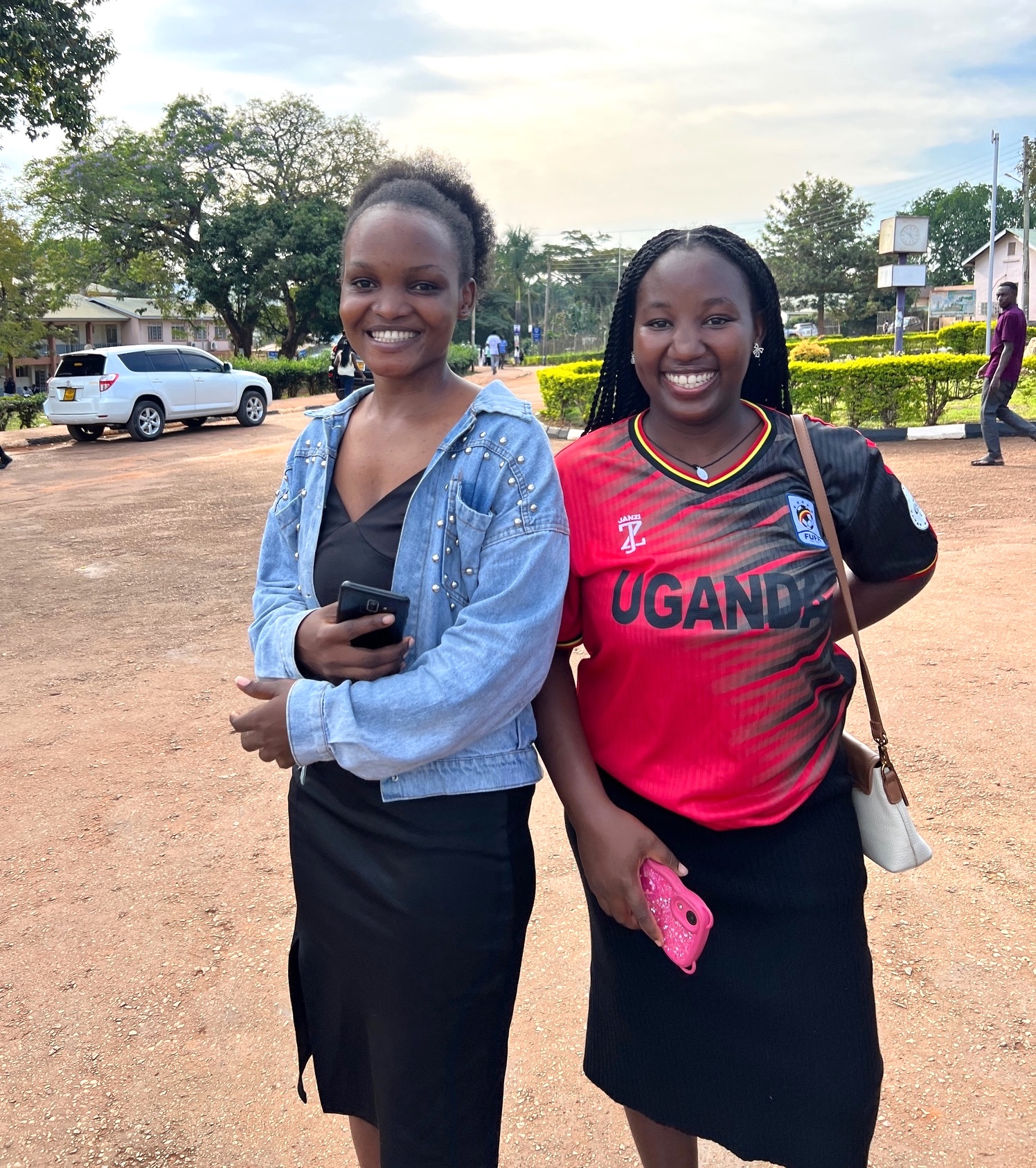 two smiling Ugandan young woment with a university campus in the background