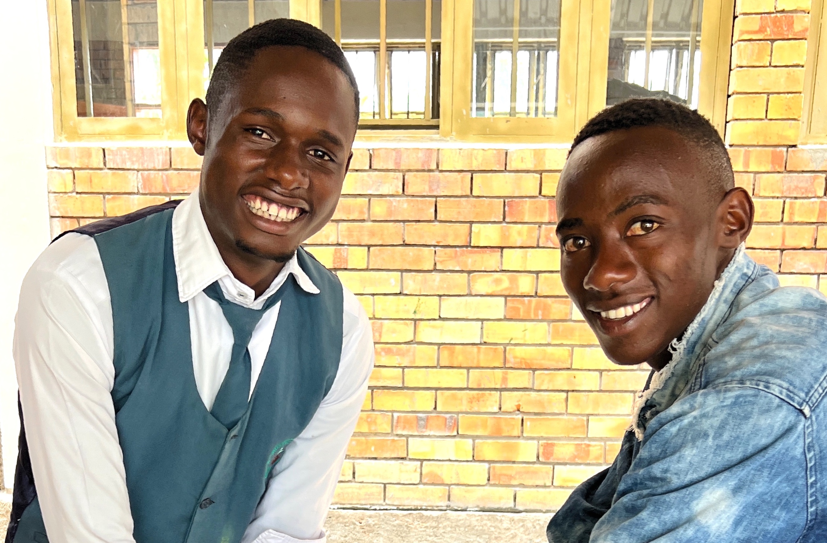 Three third-grade Ugandan boys in school uniforms are greeting visitors through an open lassroom window