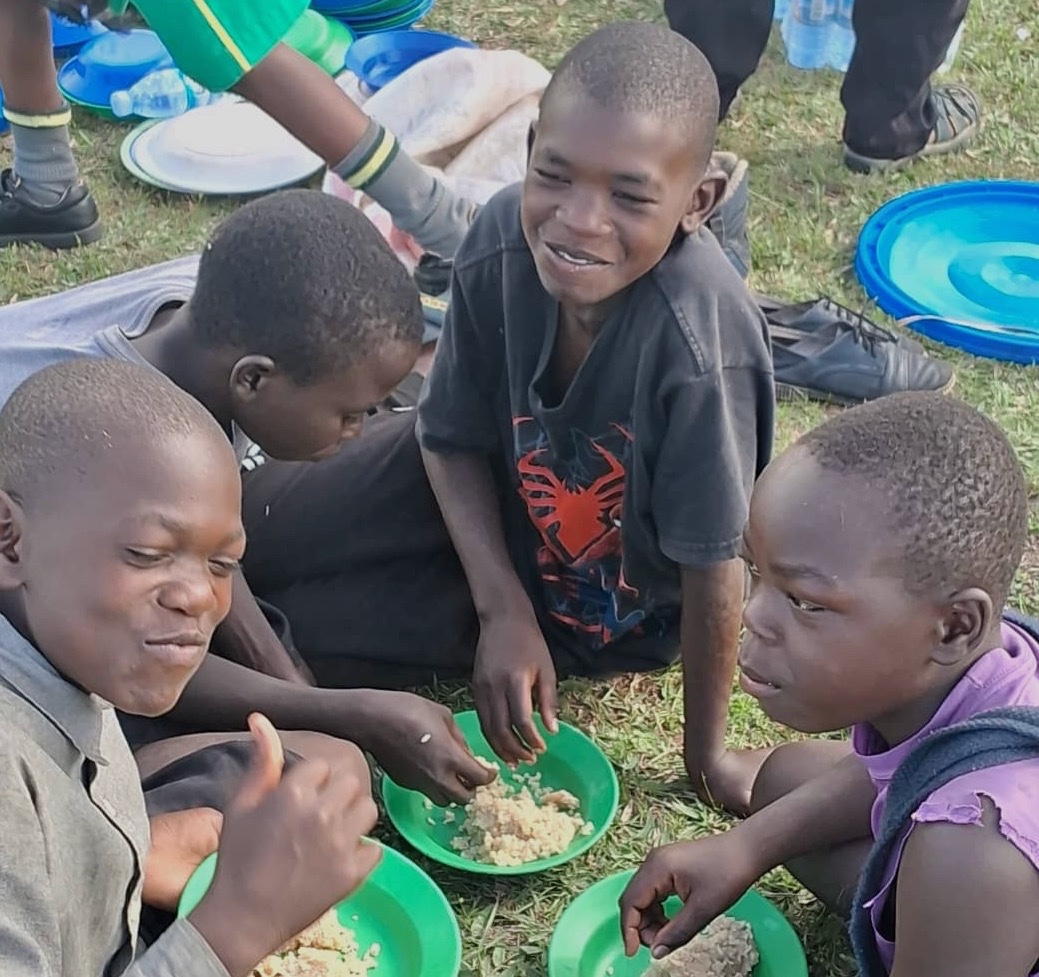 a group of young, smiling Ugandan students sitting on the ground and eating 