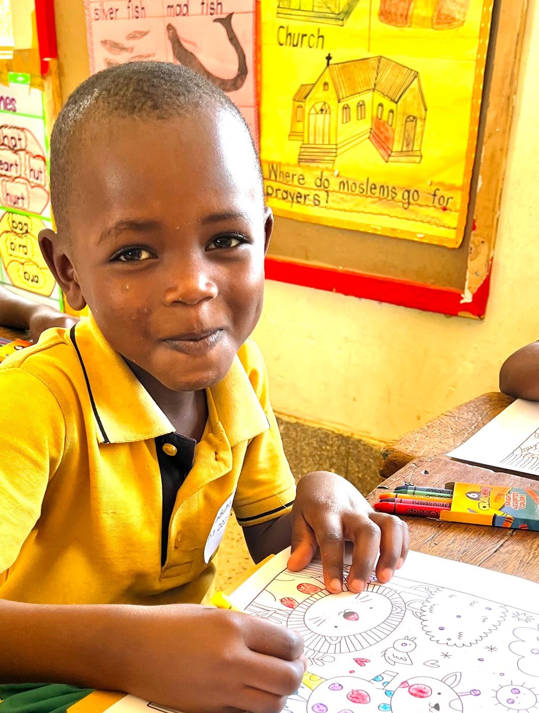 A small smiling Ugandan child coloring a giraffe