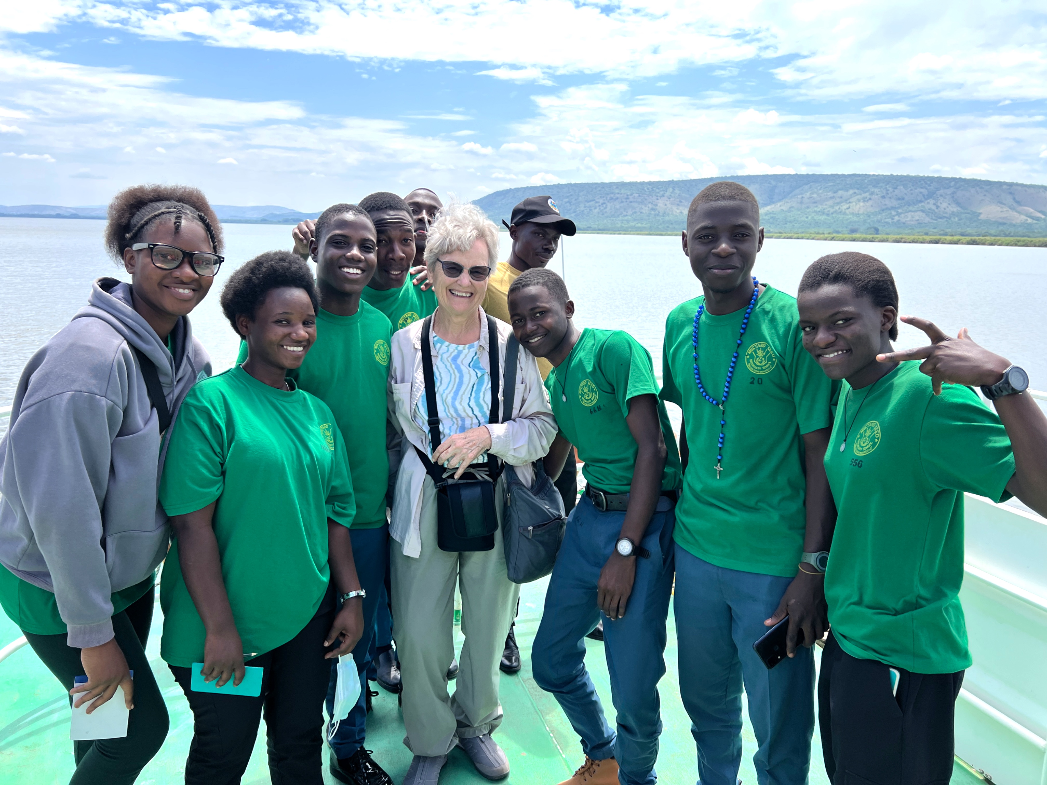 9 smiling Ugandan teens with a grey-haired, white woman on a boat