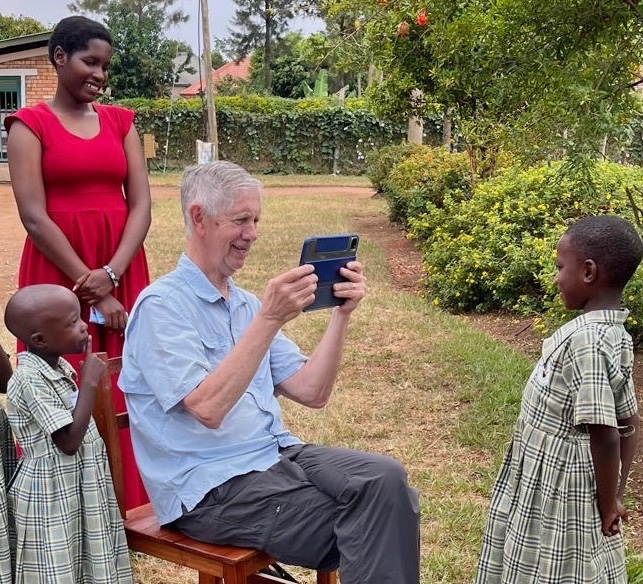 A grey-haired man taking a photo of a young student with another child and a young adult woman