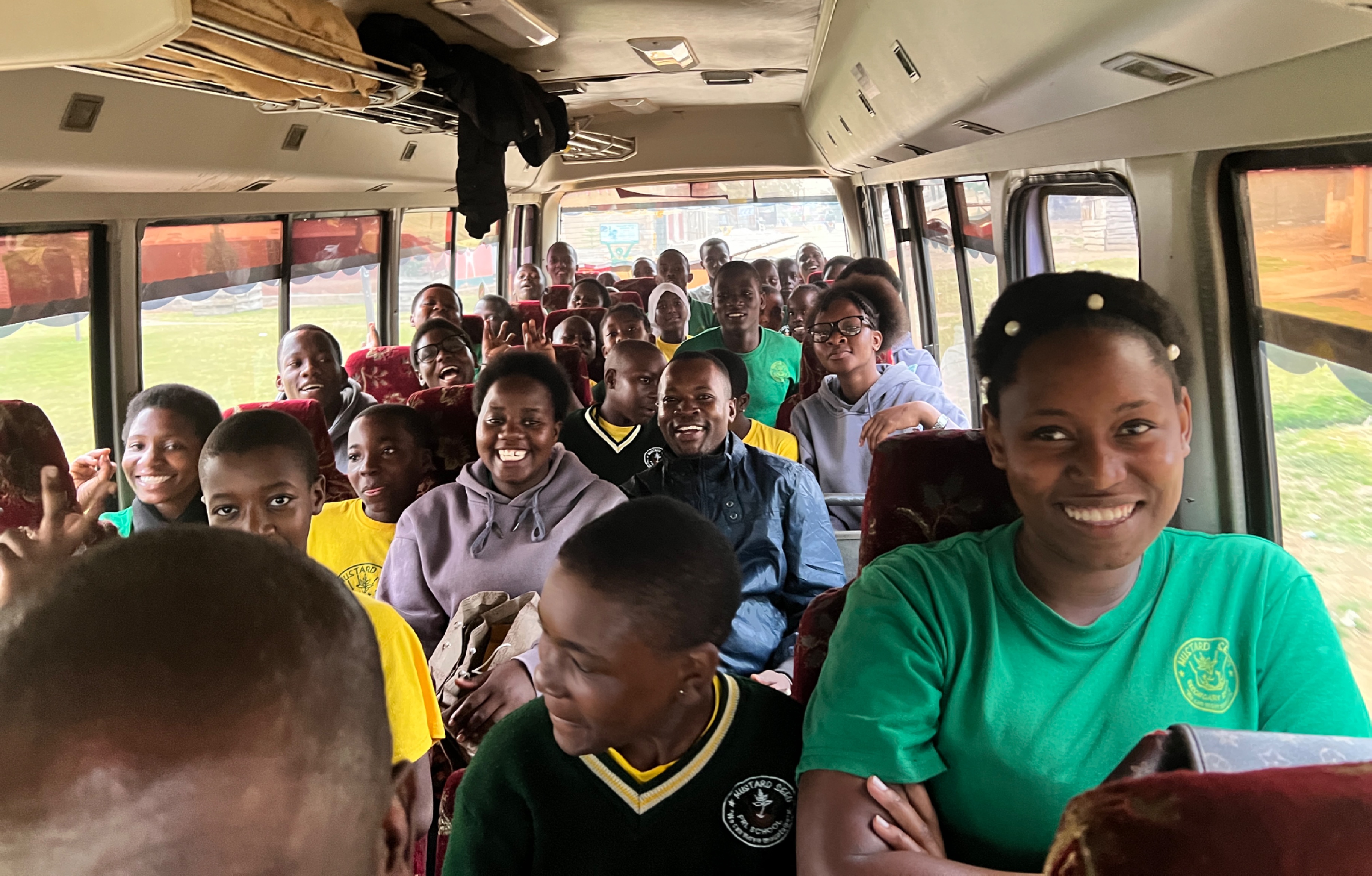 Many smiling young and older Ugandan students on a bus