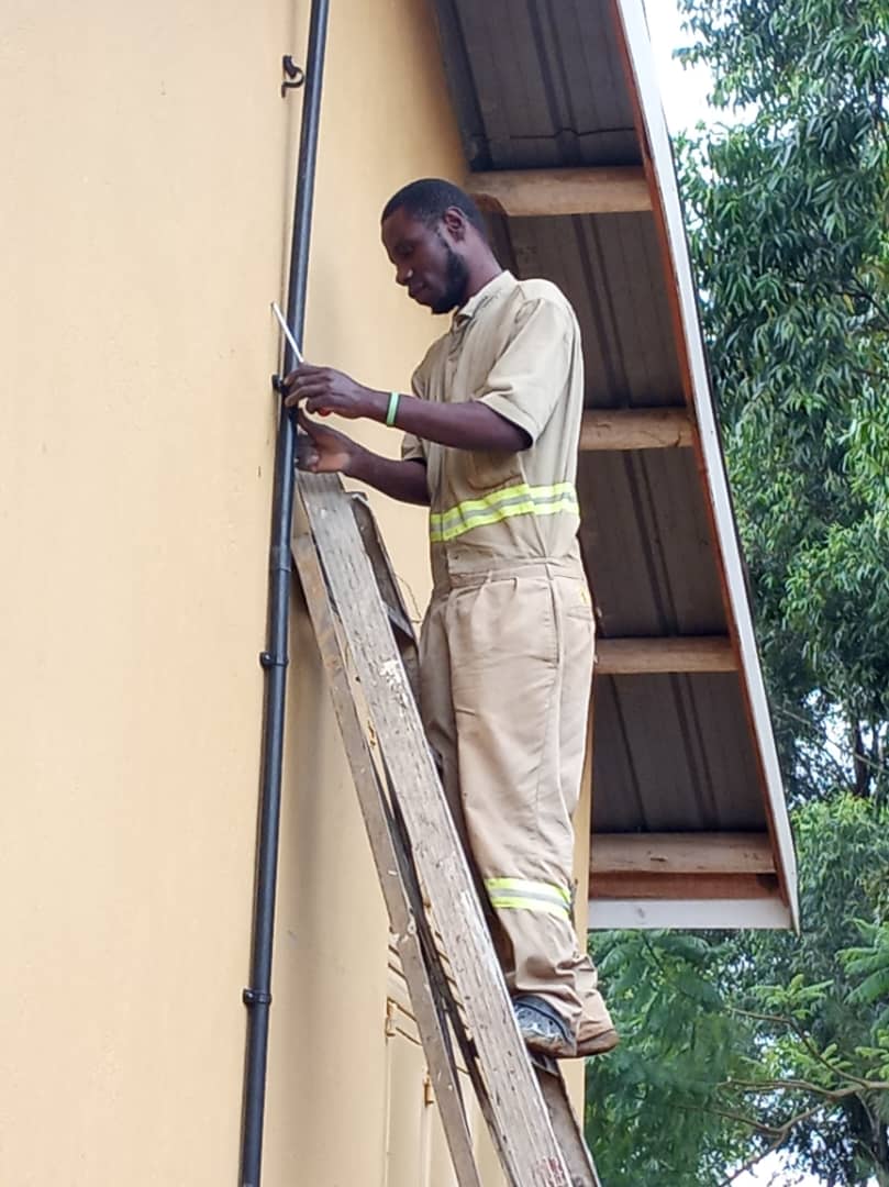 An electrician installing a lightning rod on the side of a school building in Uganda