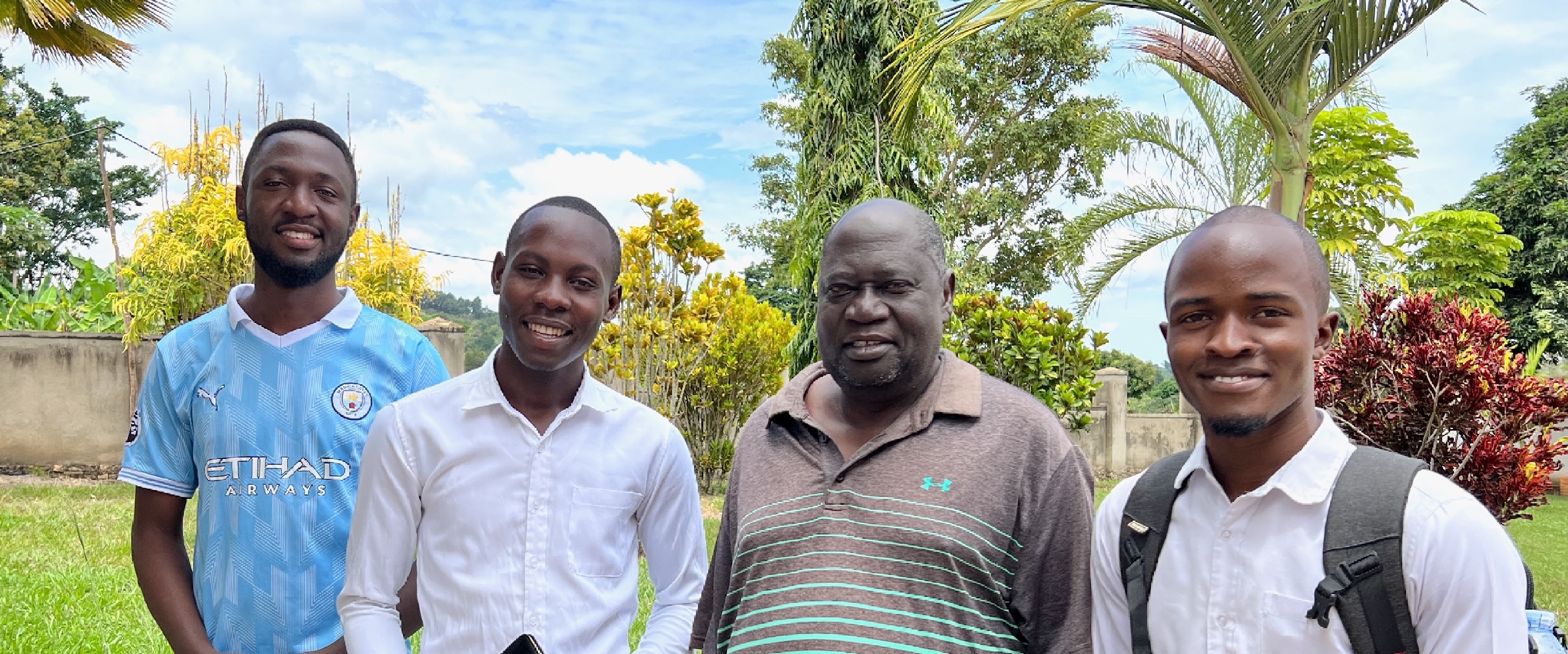 Three young Ugandan men with an older man with beautiful trees and shrubs in the background