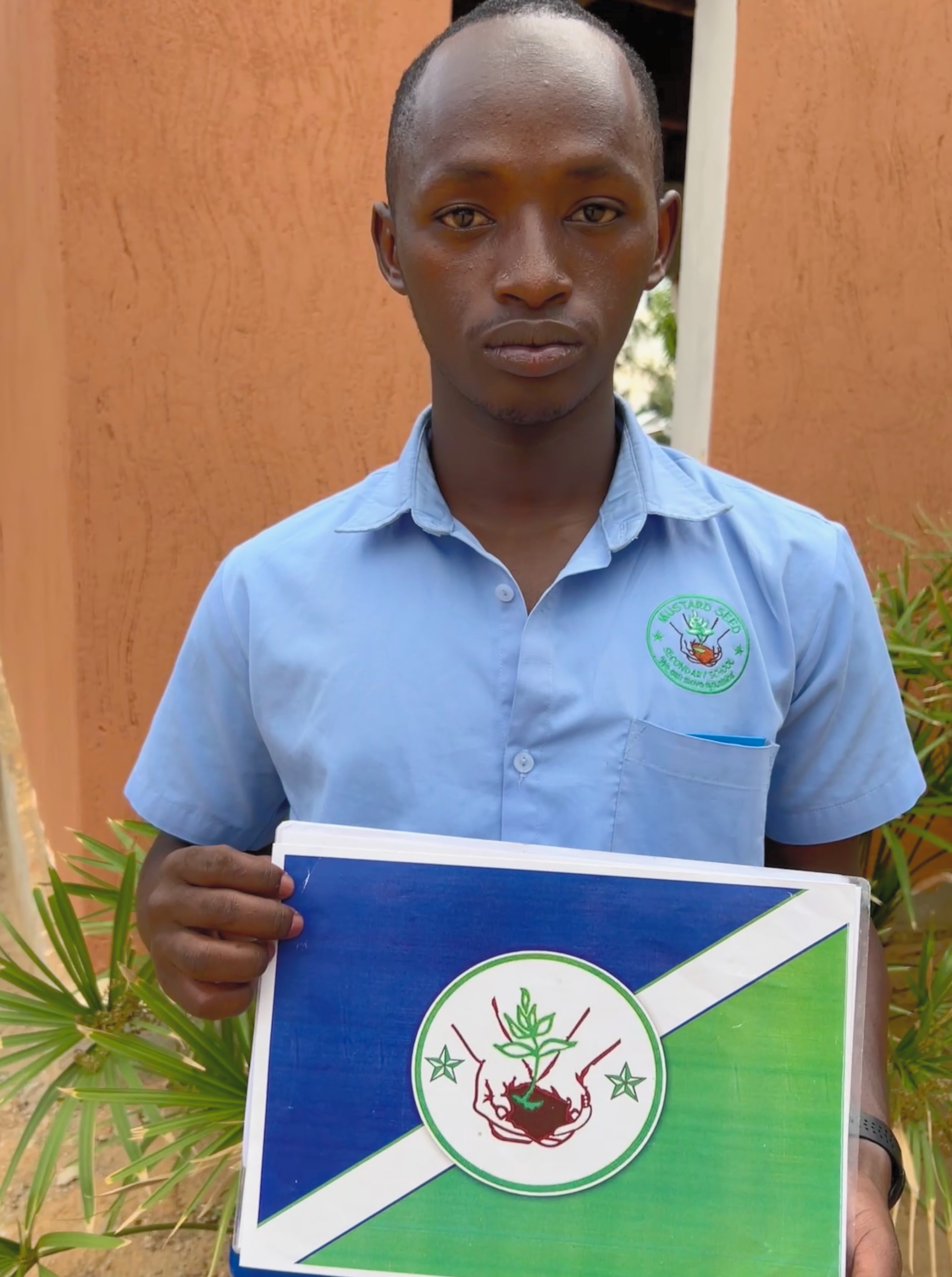 A Uganan high school student holding a blue and green design