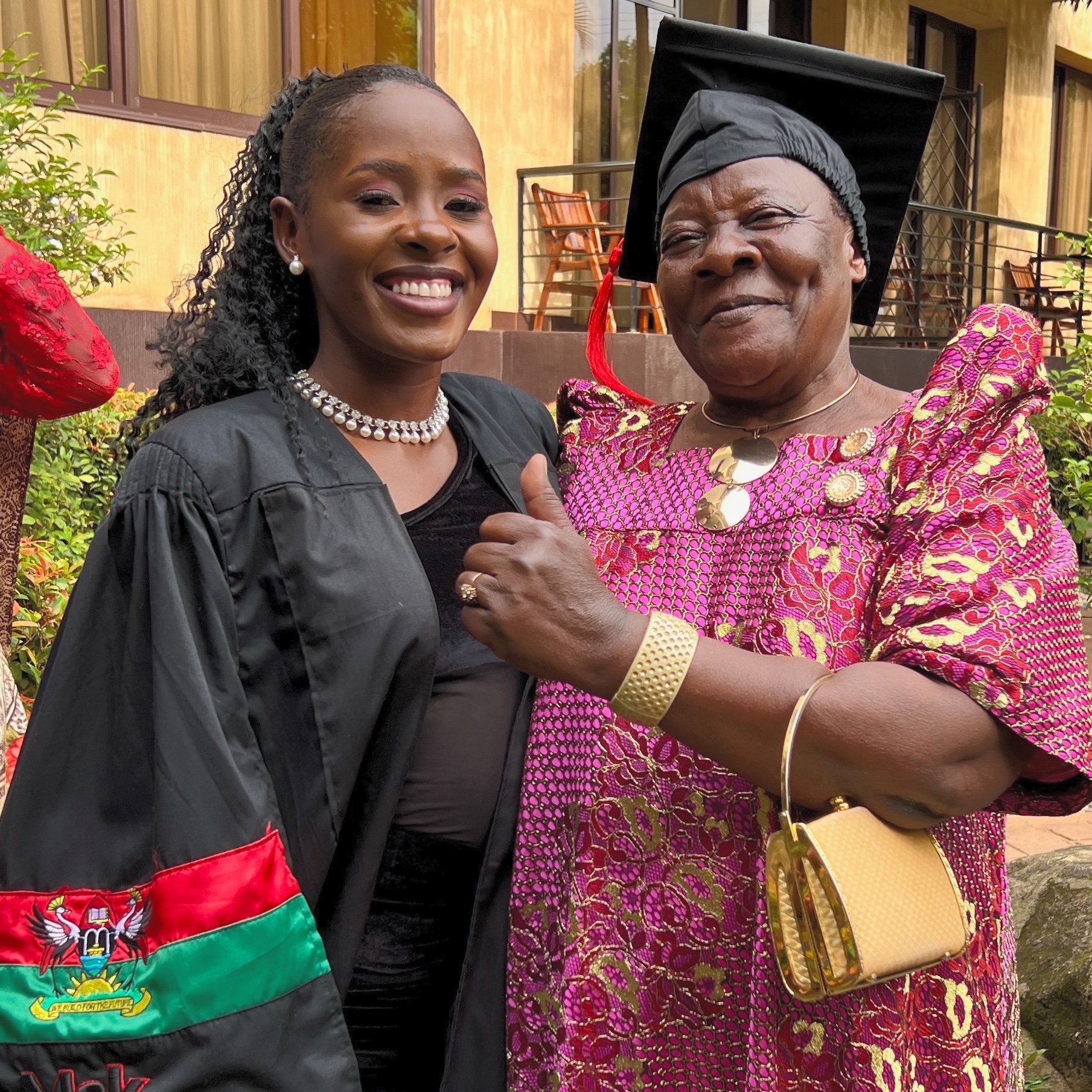 Young woman in graduation gown with grandmother wearing her graduation cap