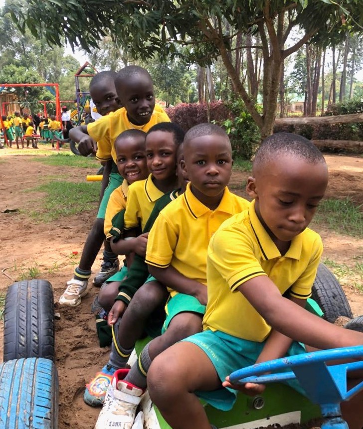 5-yr-old children on a playground 'train' with other chiildren in the background on swings, slide, etc.