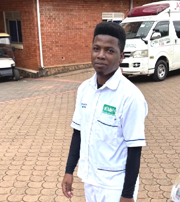 A young man dressed in a white uniform with a hospital and ambulance in the background.