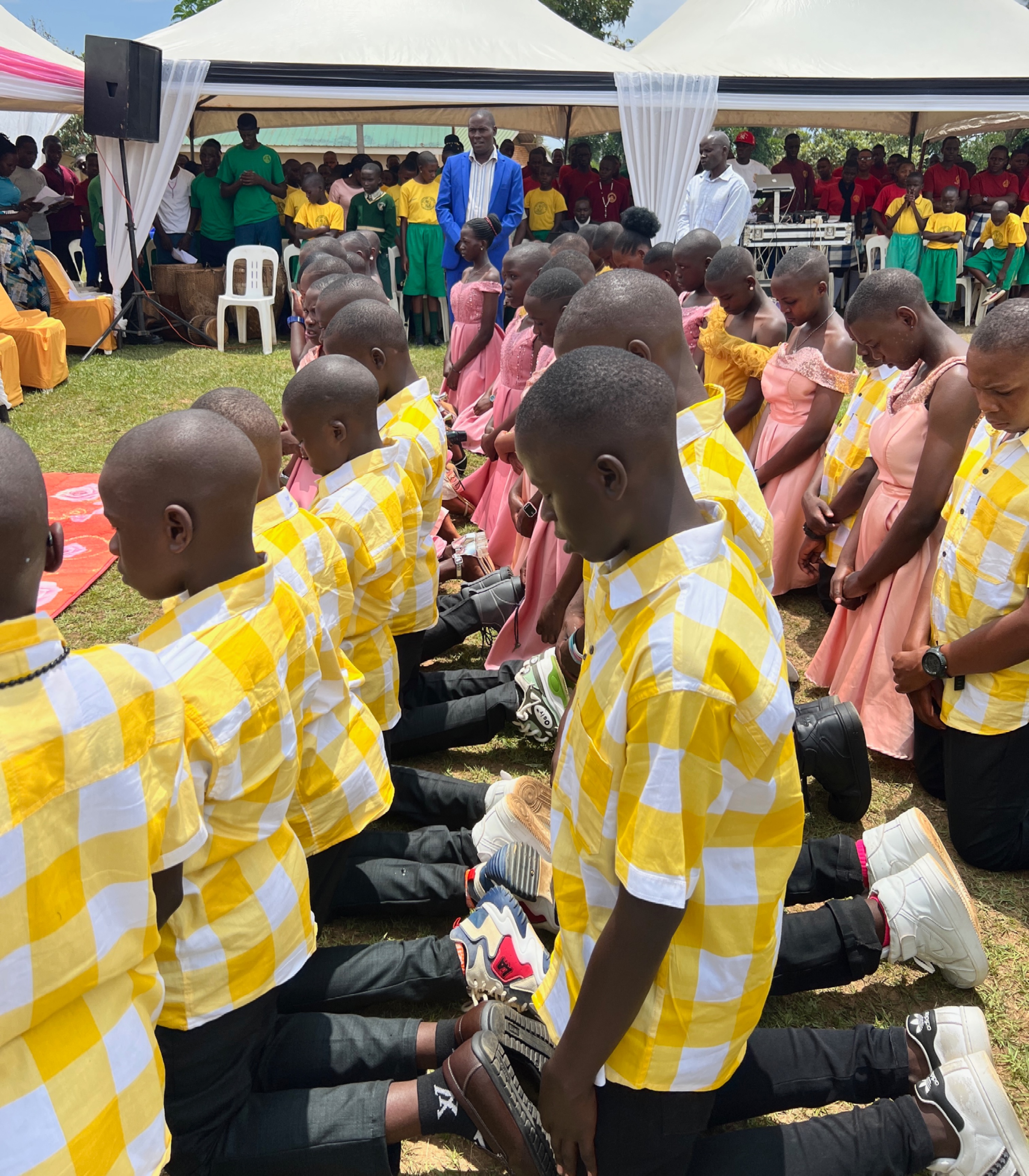 Gayly dressed Ugandan students kneeling on the grass for a blessing