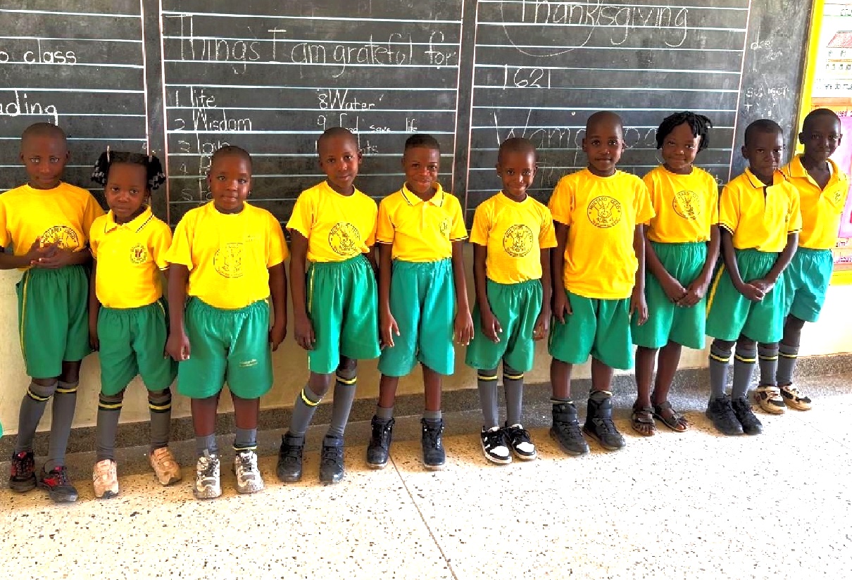 A Ugandan woman sitting at a treadle-style sewing machine along the side of the road while mending green fabric clothing