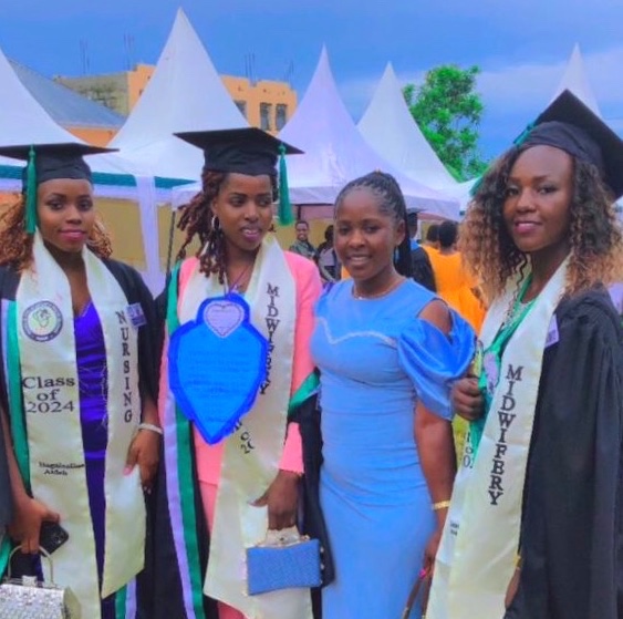 Three young women in graduation caps and gowns with another slightly older woman 