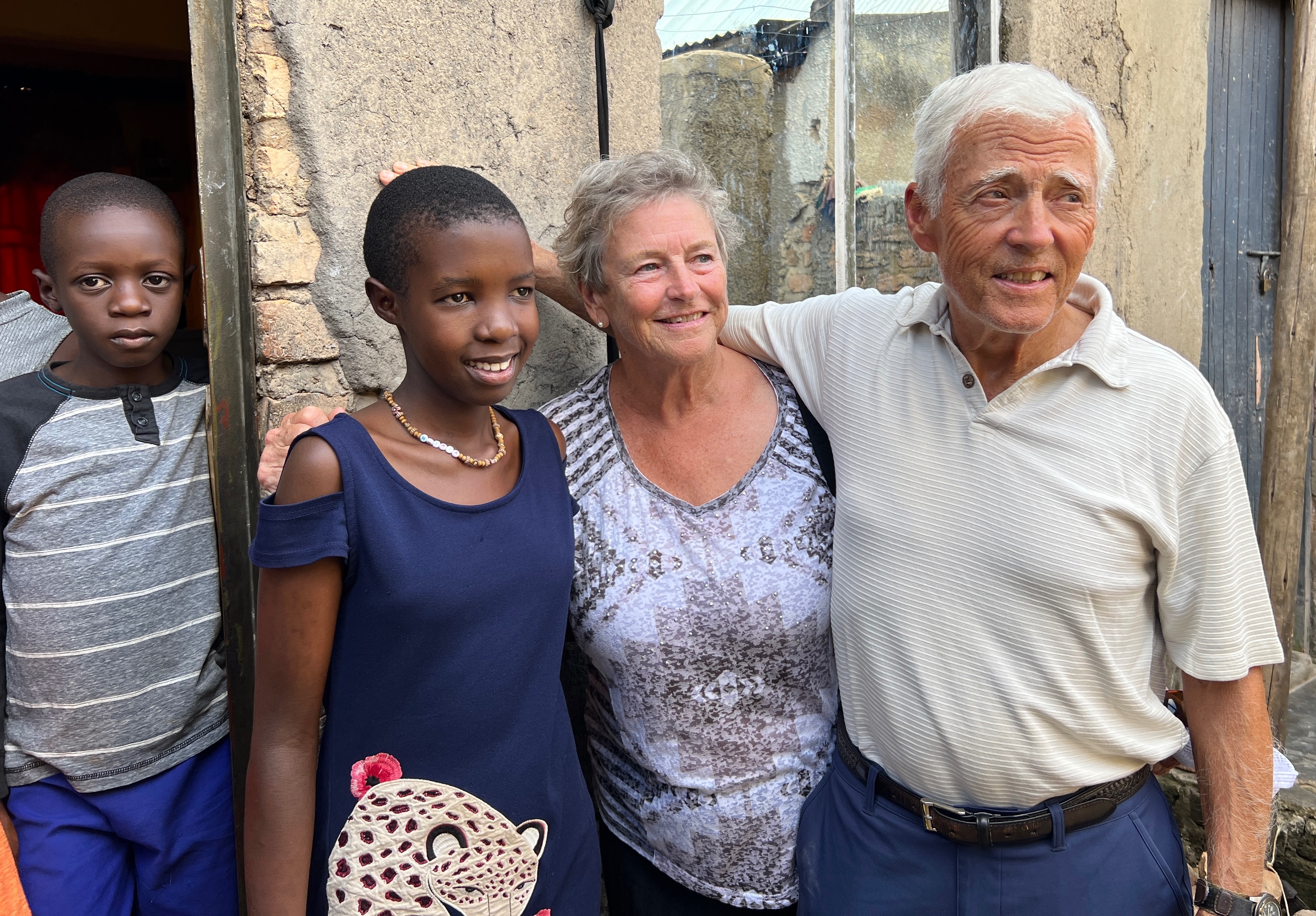 Two Americans with a Ugandan girl and her brother in front of the family's home.