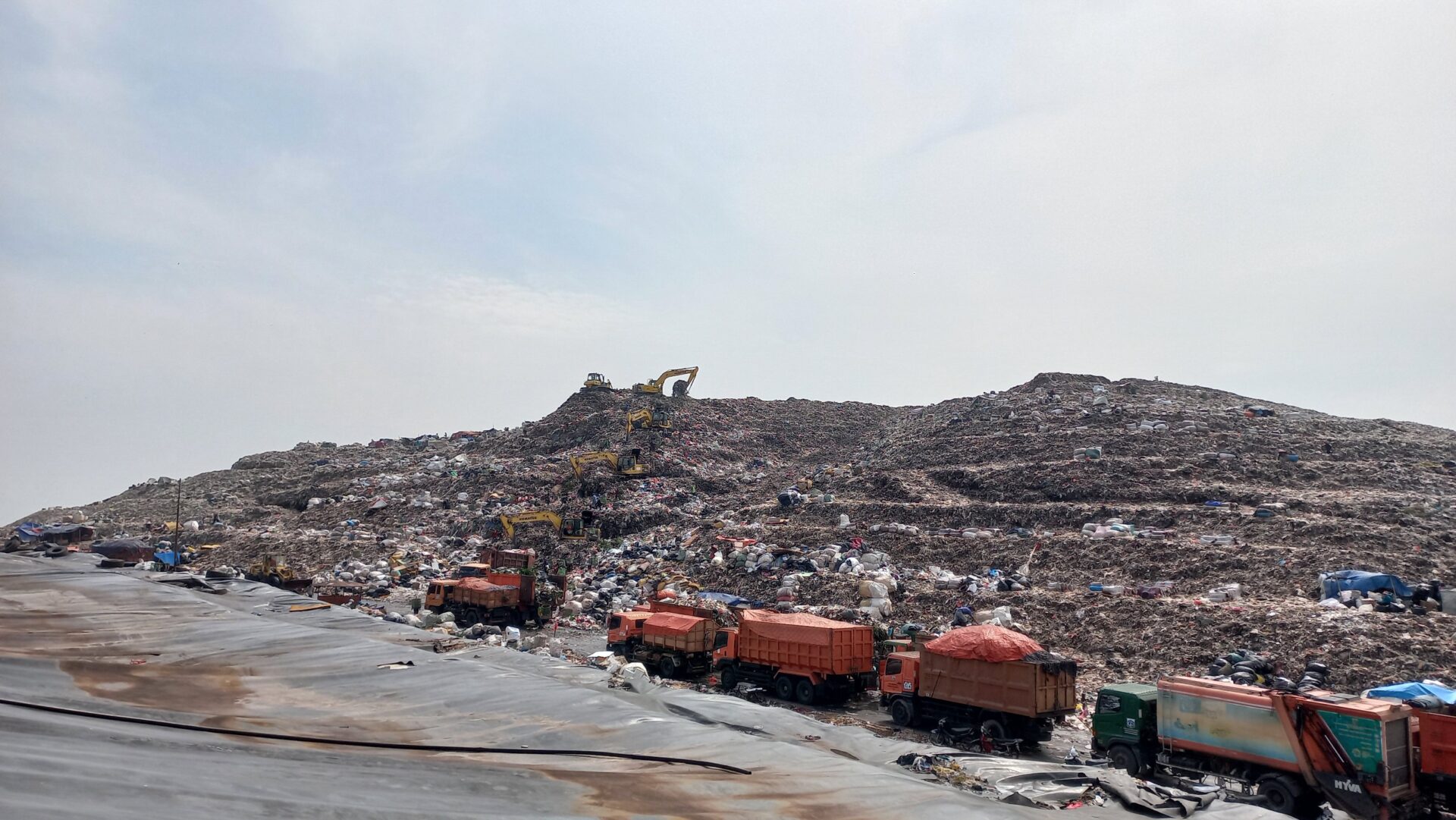 A large landfill site with waste piled high, surrounded by garbage trucks and excavators. 