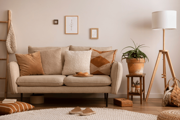 Bright, modern living room with neutral tones, a plush sofa, indoor plants, a patterned rug, and layered lighting creating a cozy ambiance